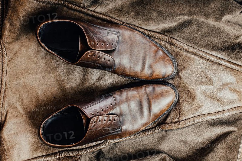 Overhead view of brown leather shoes on a rustic jacket, conveying a vintage feel