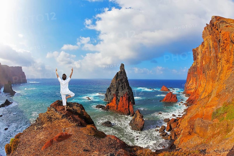The woman ashore in a white suit for yoga carries out a pose Tree. Atlantic storms. Colorful pinnacles lit sunset. Arid eastern tip of the island of Madeira
