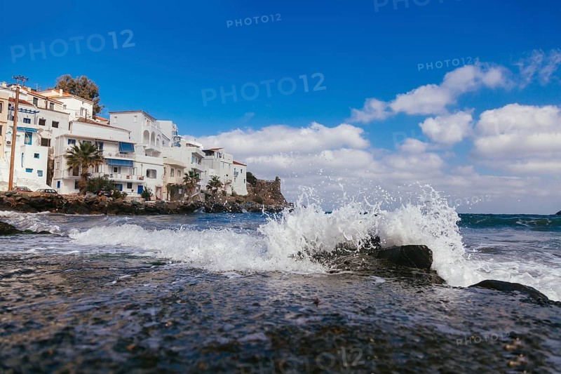 Sea wave with splashes and white houses near seashore at geek island