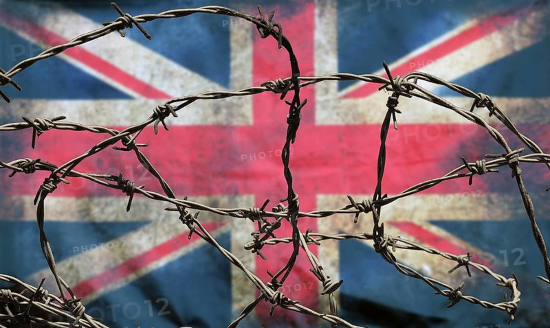 Barbed wire in front of an old stained dirty union jack british flag with dark crumpled edges brexit freedom of movement isolationist concept