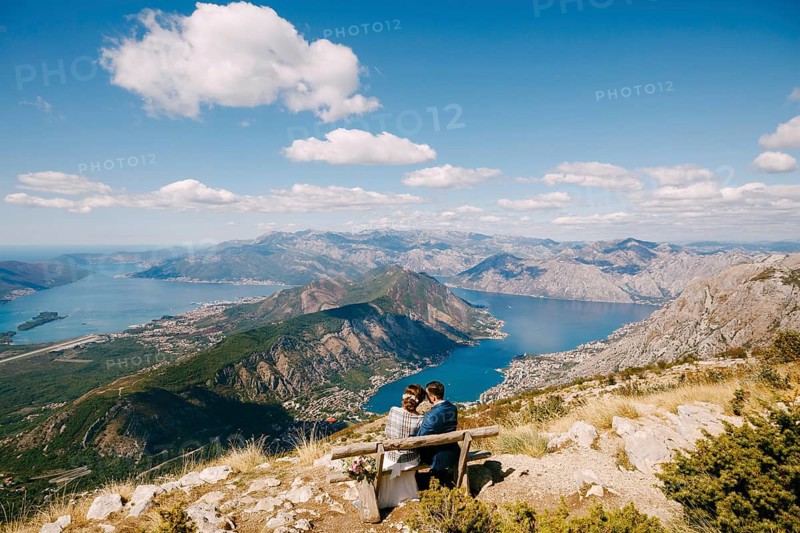 Bride and groom are sitting on a bench and looking at the Kotor bay. Excellent view from the mountains of Montenegro.