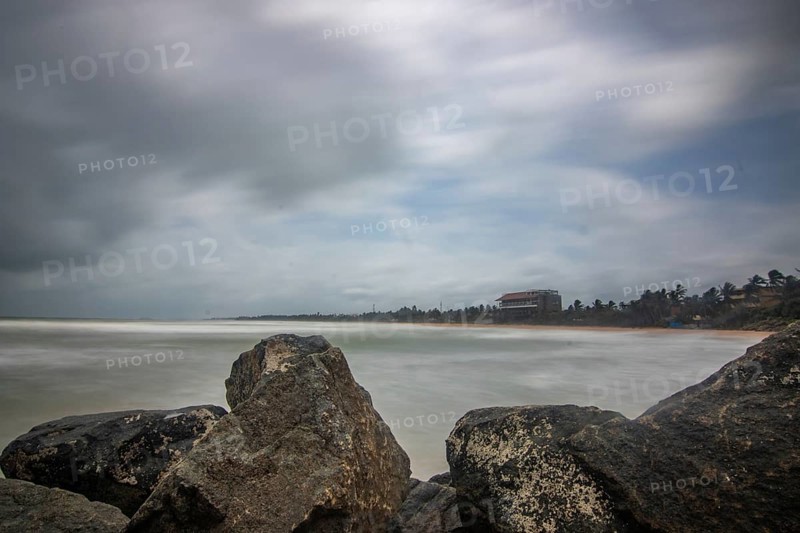 Beach, with lava rocks and vegetation, view of the sea in the evening at sunset. Landscape with clouds in Induruwa, Bentota Beach, Sri Lanka, India, Asia