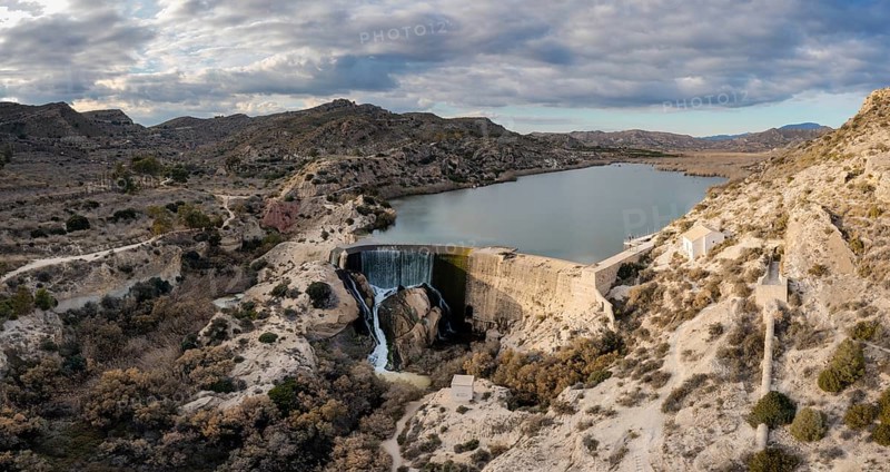 A drone view of the Elche Reservoir and dam wall with waterfall and surrounding semi-desert landscape