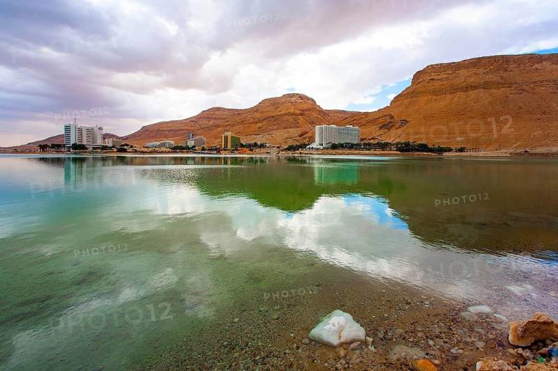 Quiet windless winter day. The smooth surface of the very salty sea water reflects the sky and clouds. Legendary Dead Sea. Israel