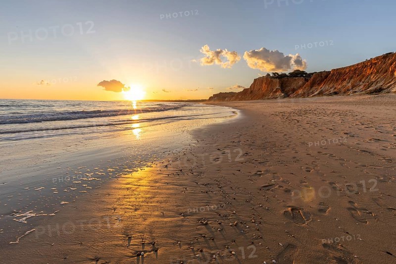 Beautiful sandy beach with red rocks and cliffs. Twilight at sunset with shallow waves on the Atlantic coast in Praia do Poço Velho, Praia da Falésia, Algarve, Portugal, Europe