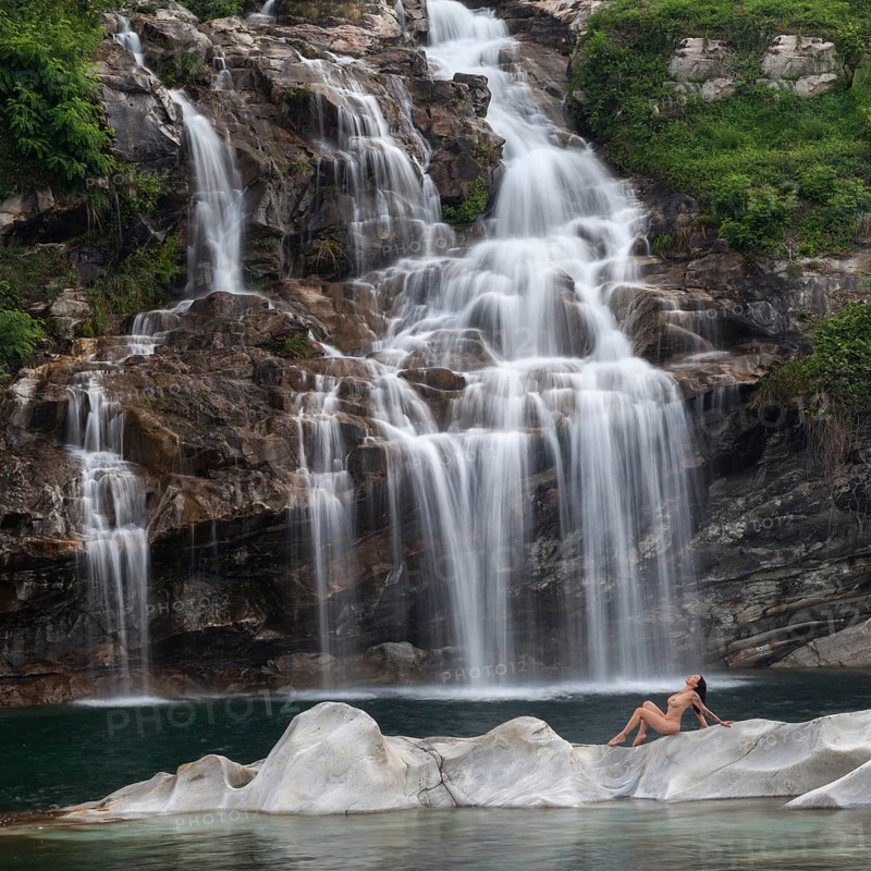 Professional model in elegant pose on a rocky island in front of an impressive waterfall, Aesthetic Nude Photography Outdoor Shooting, Maggia, Maggia Valley Canton Ticino, Switzerland, Europe