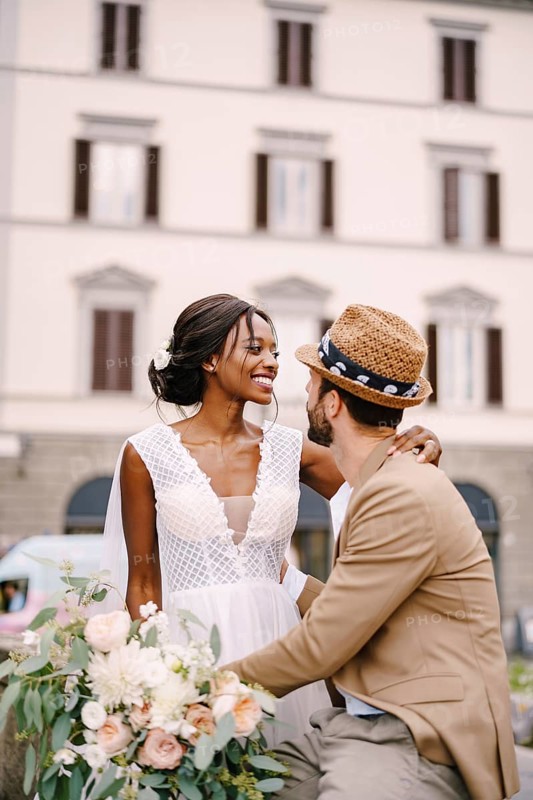 Multiracial wedding couple. Wedding in Florence, Italy. African-American bride in a white dress with a long veil and a bouquet, and Caucasian groom in a sandy jacket and straw hat