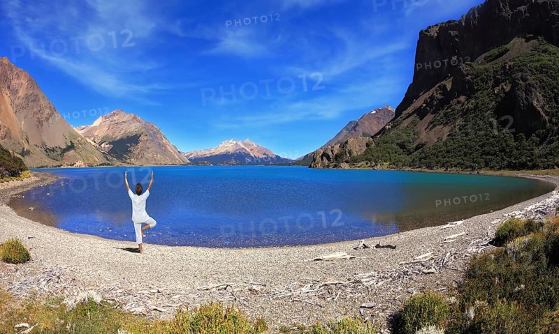 Yoga on the lake. Mature woman in white performs asana tree, standing on the shore of round lake