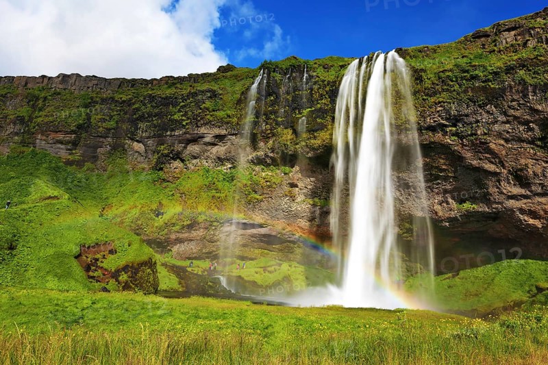 Sunny day in July. Seljalandsfoss waterfall in Iceland. Large rainbow decorates a drop of water