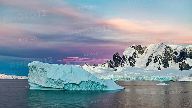 Iceberg floating in the sea in front of a snow-covered mountain backdrop at sunset, icebergs in the Southern Ocean in Antarctica