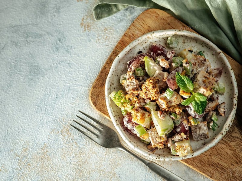 Waldorf salad with copy space. American fruit and nut salad with apples, celery, grapes, chicken meat, dressed mayonnaise. Craft plate with ready-to-eat waldorf salad on gray background. Top view