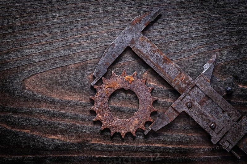 Rusty retro-styled measuring calipers with pinion gear on vintage dark wooden background construction concept