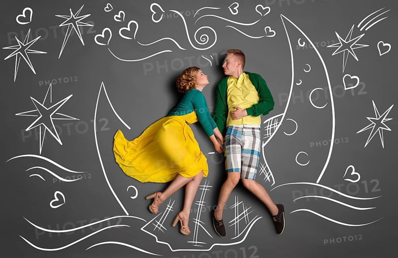 Happy valentines love story concept of a romantic couple swimming on the moon boat, holding hands and kissing against chalk drawings background of a night sky