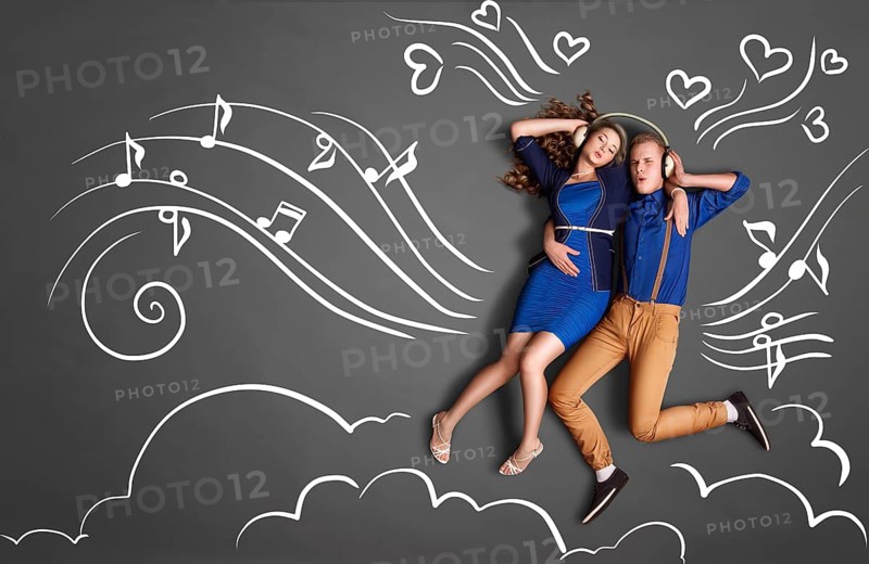 Happy valentines love story concept of a romantic couple sharing headphones and listening to music against chalk drawings background of notes, player icons and clouds
