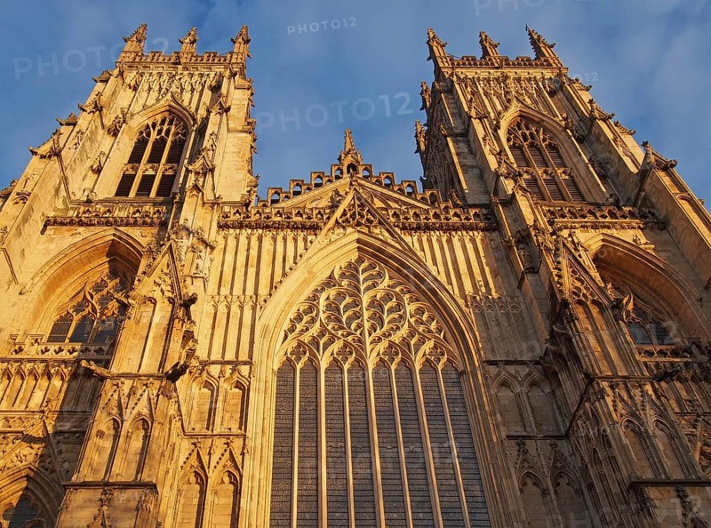 A front view of the towers at the entrance to york minster in sunlight against a blue cloudy sky