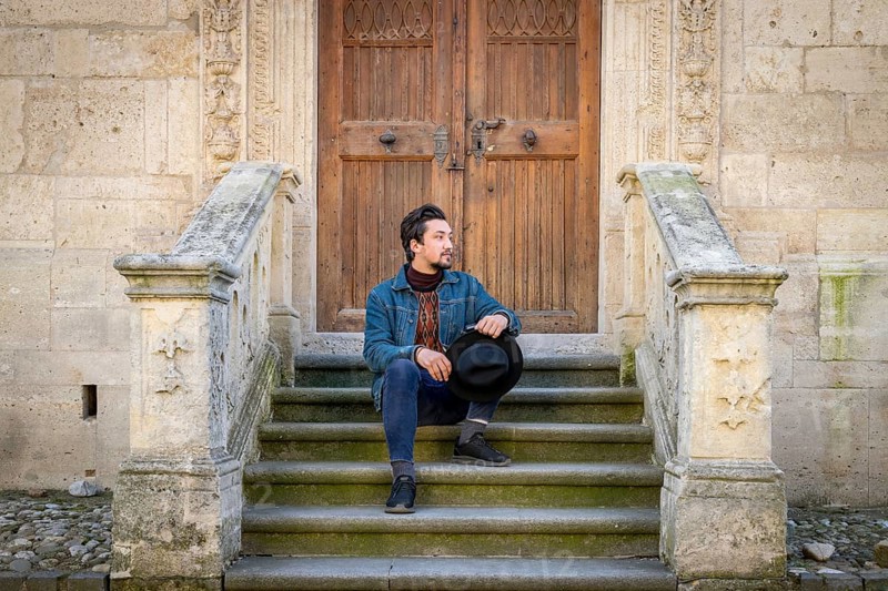 Portrait of a young man sitting against a beautiful old medieval cathedral door. A man in front of a an old architecture church entrance door in Alba Iulia, Romania, Europe