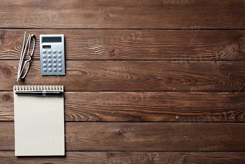 Still life of accountant workspace with office accessories. Flat lay wooden desk with elegant glasses, calculator and spiral notepad. Accounting and banking services. Finance and investment concept