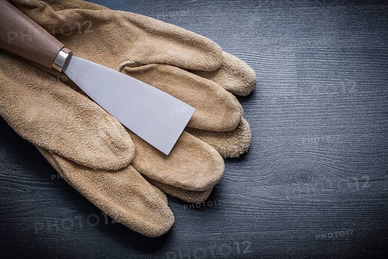 Single paint scraper on working glove and wooden board