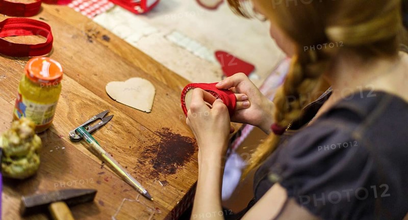 Brown-haired woman manufacturing heart-shaped red purses on the wooden table