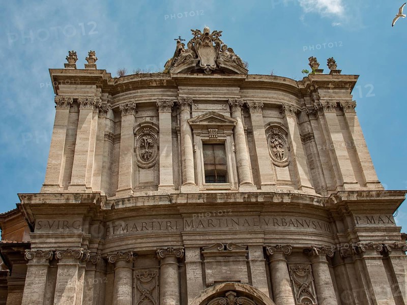 Front façade of a baroque building with intricate ornamentation and Latin inscription, framed in a blue sky, Rome, Italy, Europe