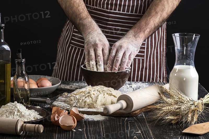 A handful of flour with egg on a rustic kitchen. Against the background of men's hands knead the dough. Ingredients for cooking flour products or dough bread, muffins, pie, pizza dough . Copy space