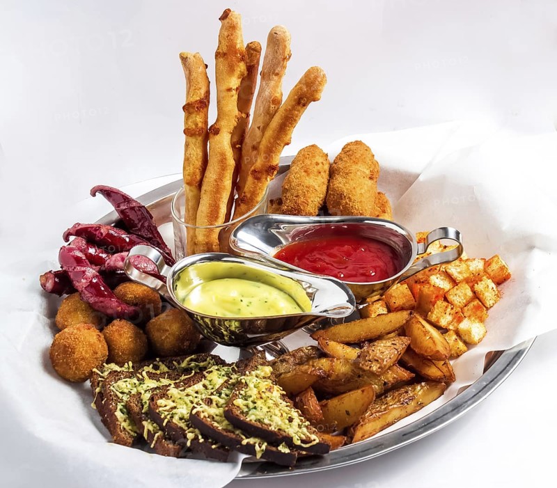 Large plate with a wide selection of snacks for beer served with two kinds of sauce on a white background