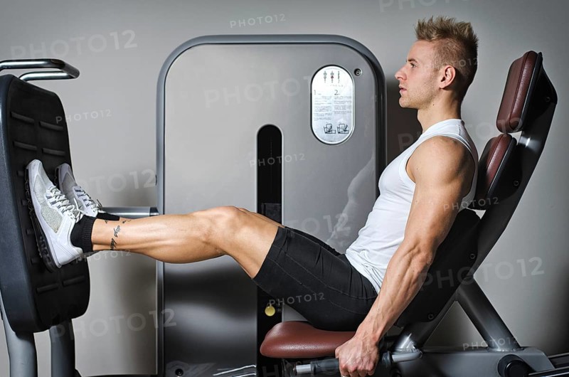 Attractive and fit young man in gym working out legs and exercising on equipment