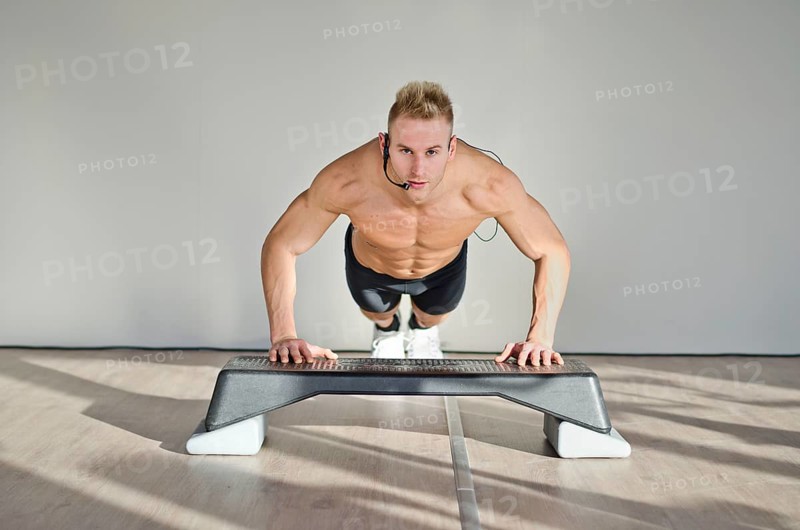 Young aerobics male coach shirtless leaning on step teaching class
