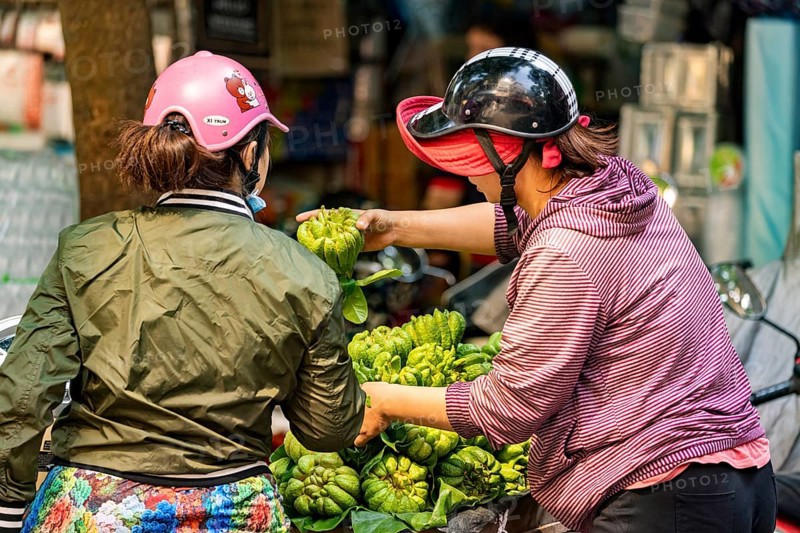 Two woman trading green fruits on Krong motorbikes in an urban environment, woman selling fruits in the streets of Hanoi Vietnam