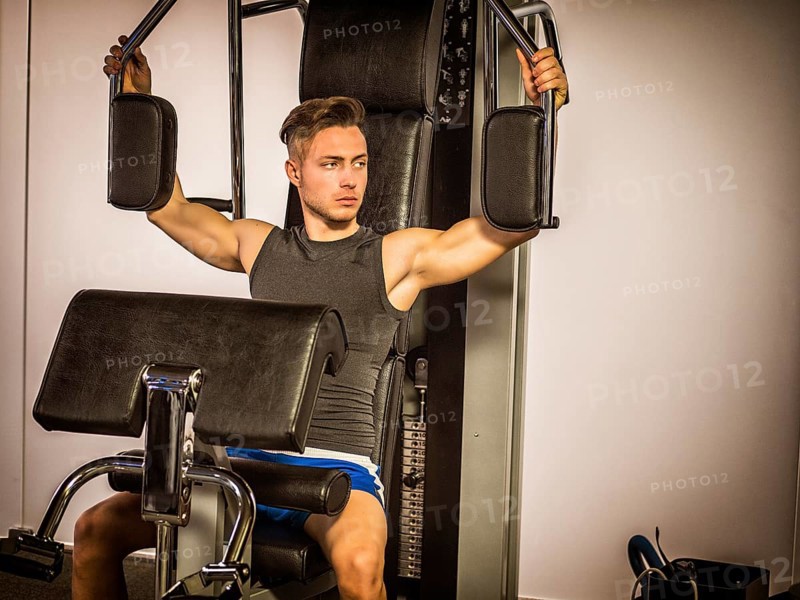 Muscular young man, training pecs on gym cable machine