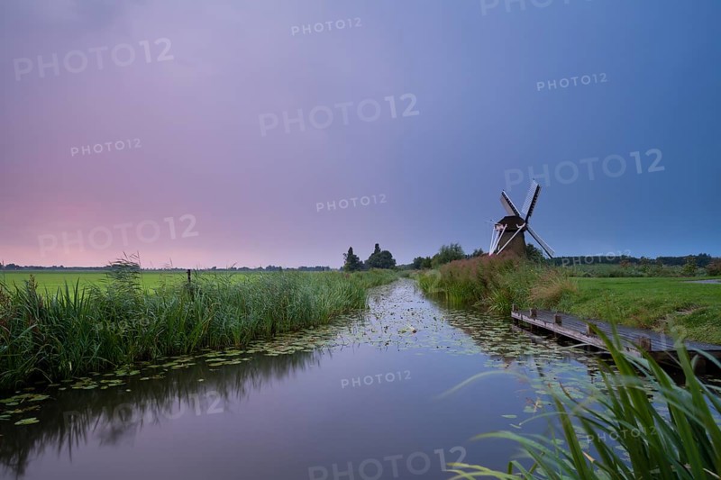 Charming windmill by river at rainy sunrise, Holland