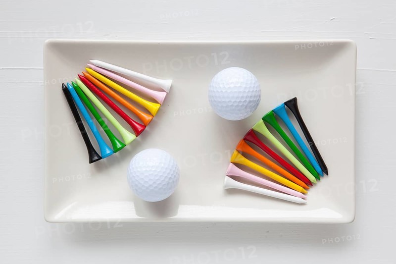 White ceramic dishes with golf balls and wooden tees on over white background, rectangle dish