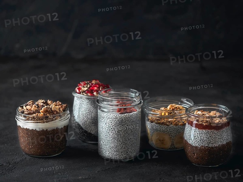 Set of chia pudding in different glass jars on dark table. Assortment of chia puding with different fruits, nuts, ingredients. Copy space for text. Superfood, detox, healthy overnight breakfast concept