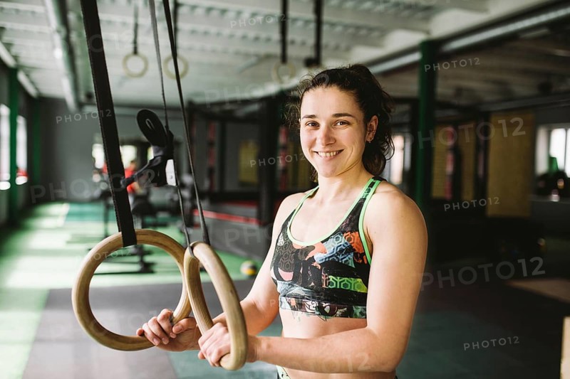 Beautiful girl doing an exercise on the gym rings in the gym. Happy and smiling