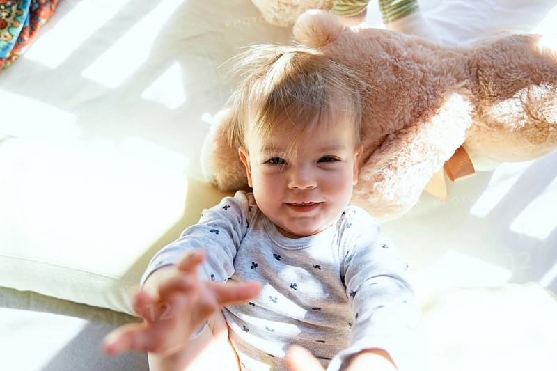 Small child lies in a wooden crib on a large teddy bear.