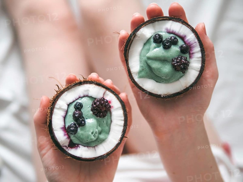 Two coconut half with smoothie or yogurt in woman hands. Blue spirulina smoothie in coconut with frozen berries. Healthy breakfast concept. Ideas and recipes for healthy vegan breakfast. Copy space