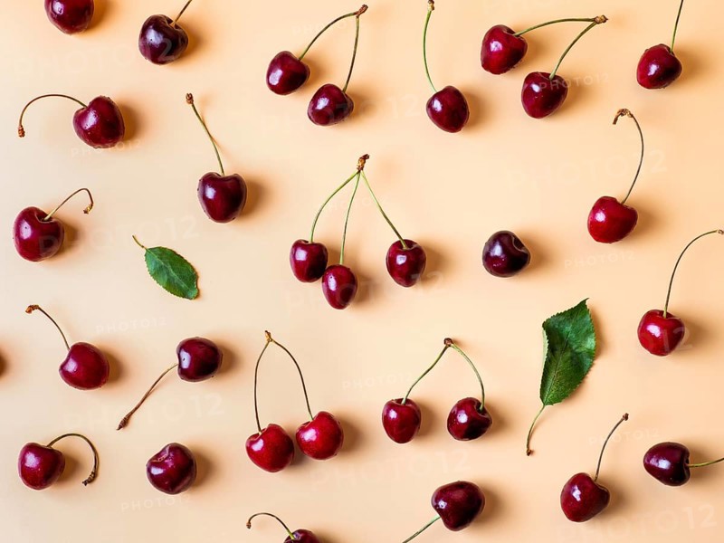 Fresh cherries scattered on yellow background. Creative fresh cherry pattern background with copy space. Top view or flat lay. Sprinkled cherry with green leaves as creative layout for food background