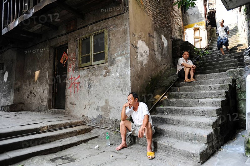 04.08.2012, Chongqing, China, Asia, Men sit on the steps in front of an old house in the old town of Shibati, on whose wall red letters inform the residents about the imminent demolition of the building to make room for new buildings, Asia