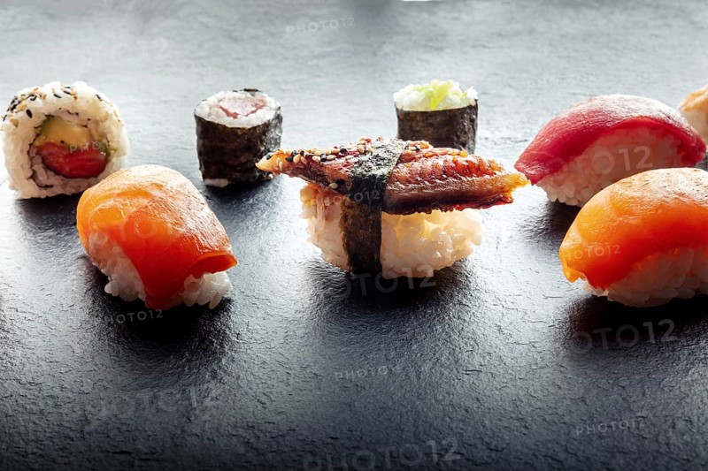 Sushi on a black slate plate. Nigiri with eel, salmon and tuna, roll with avocado and maki with cucumber on a black background, Japanese food on a plate at an Asian restaurant, Food photography, Food photography