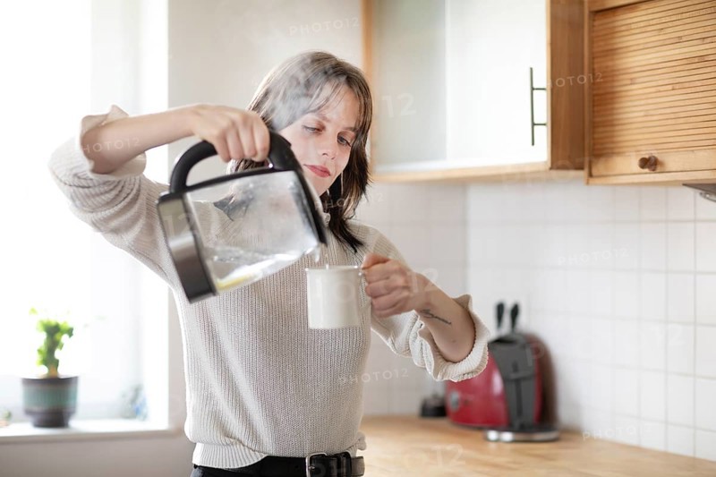 Woman pouring water into a cup in a bright kitchen with kettle, energy-saving, environmentally friendly