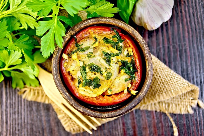 Fish baked in tomato in Zandvoort in clay bowl on a napkin of burlap, parsley on a dark wooden board on top