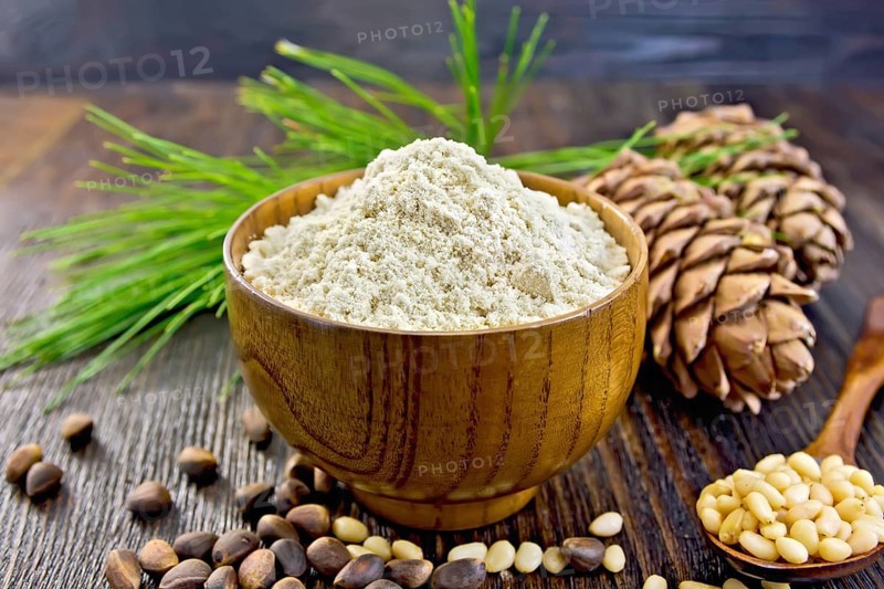 Flour cedar in a wooden bowl, cedar nuts and two cones, a spoon with peeled nuts, cedar branch against the backdrop of wooden planks