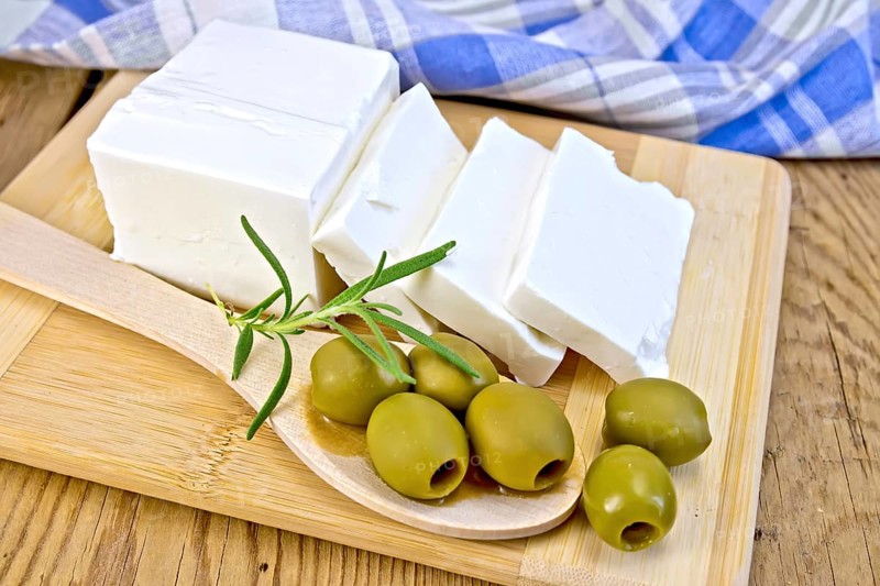 White brine cheese, rosemary, olive in spoon, blue plaid napkin on a wooden boards background