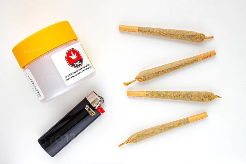 Calgary, Alberta, Canada. Aug 19, 2020. A Cannabis white and yellow plastic packaging container with Cigarettes, Prerolls or Joints and a lighter on a white background