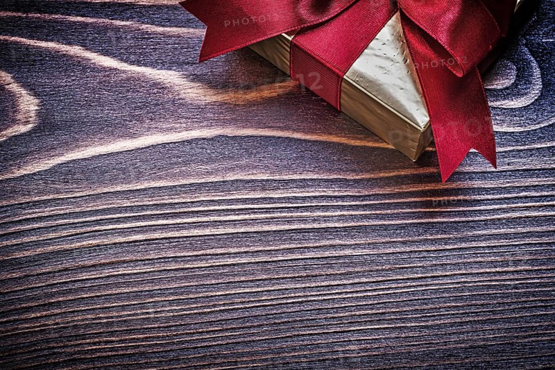 Present box with red satin ribbon on wooden board