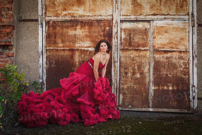 Woman in cloudy red dress is posing over rust wall. Fashion portrait without retouch, only make up