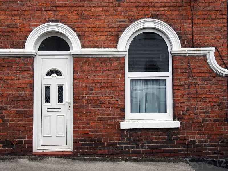 White front door and window of a typical old brick british terraced house with white decorative paintwork