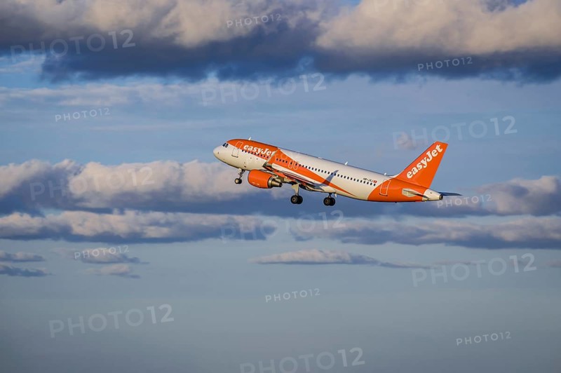 Lisbon, Portugal - Apr 29, 2024: EasyJet Airbus 320 aircraft shot mid-flight, ascending into clear blue sky with some clouds after takeoff on sunny day. Air traffic, vacations, travel, destinations, aircraft, low-cost airline, commercial flight
