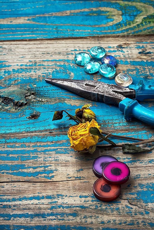 Beads, pliers, and other needlework accessories on outdated turquoise wooden background