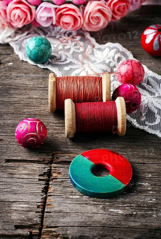 Beads and spool of thread, piece of lace on textured wooden background